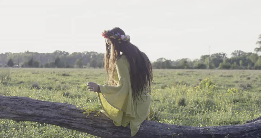 A woman sitting on a log during the day is holding a bunch of flowers
