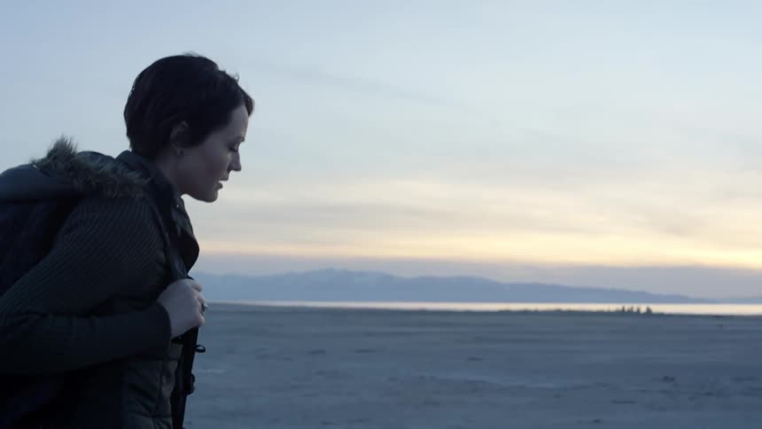 A woman wearing a backpack walks on the sand at sunset
