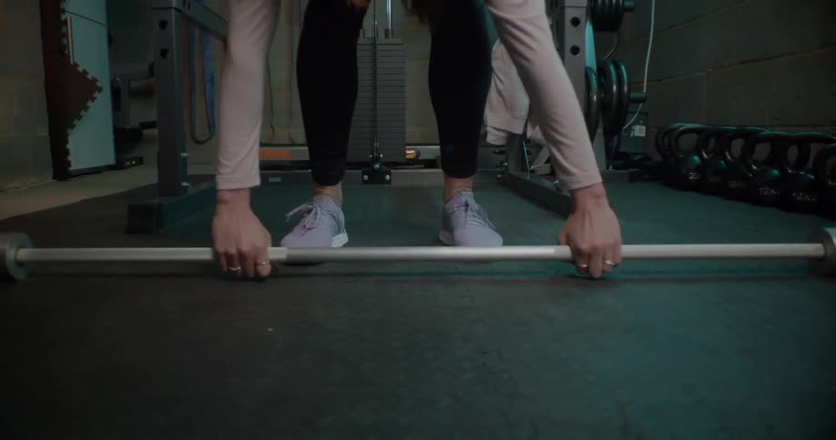 Woman bends over and picks up a barbell and then stands up