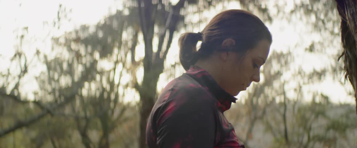 A woman looks down while standing in the woods