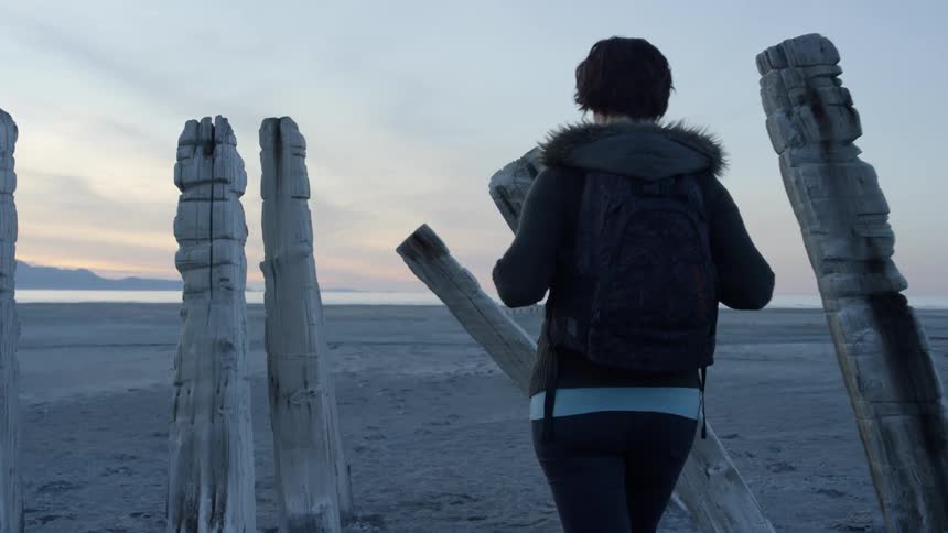 A woman is walking with a backpack on the beach towards the water