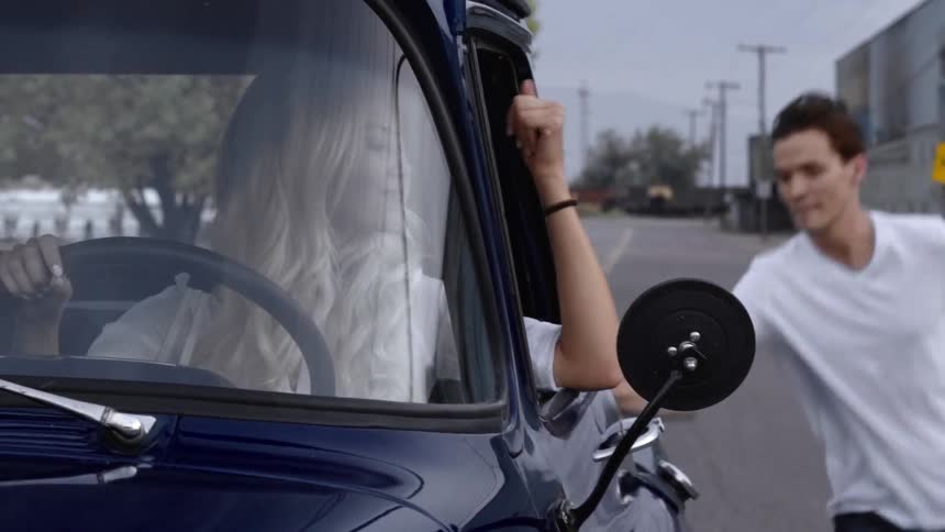 A young man walking up to a truck and jumping in the back as the blonde woman driving motions him to "come on"
