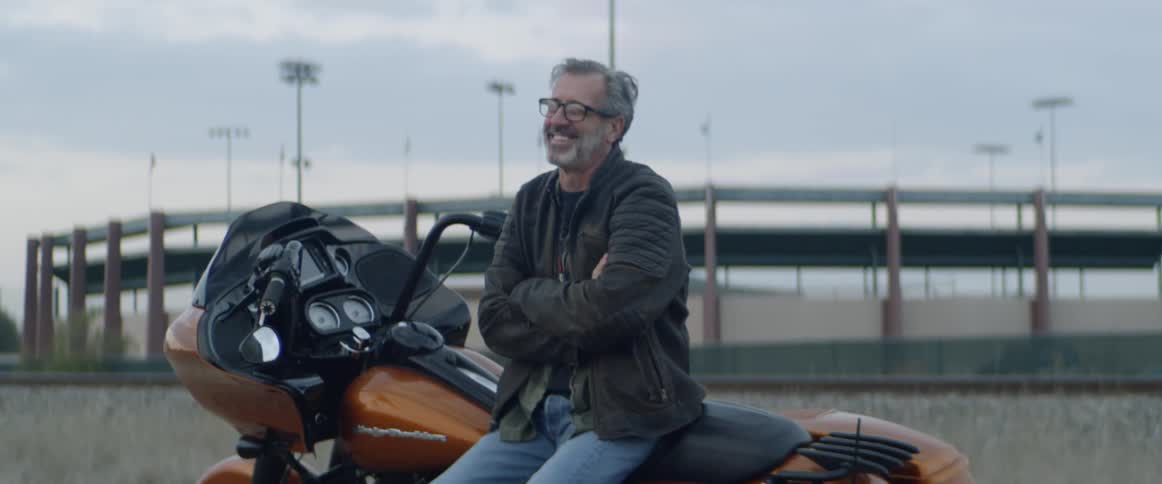 Man sits and smiles on an orange motorcycle