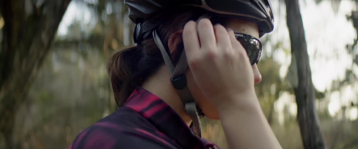 A woman wearing a helmet puts on sunglasses
