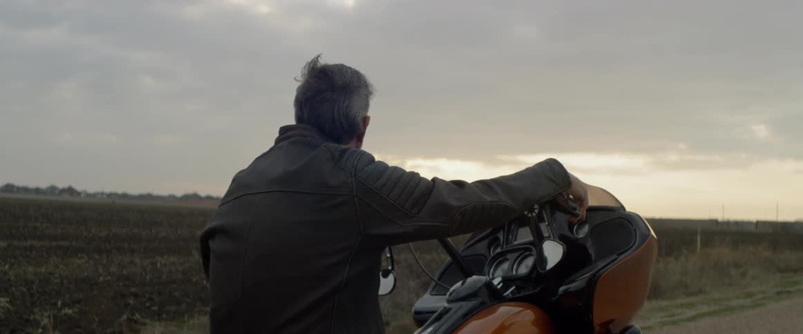 Man sits on a motorcycle as he looks towards a cloudy sky