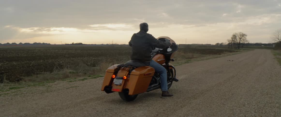 Man rides a motorcycle on a rural road at sunset