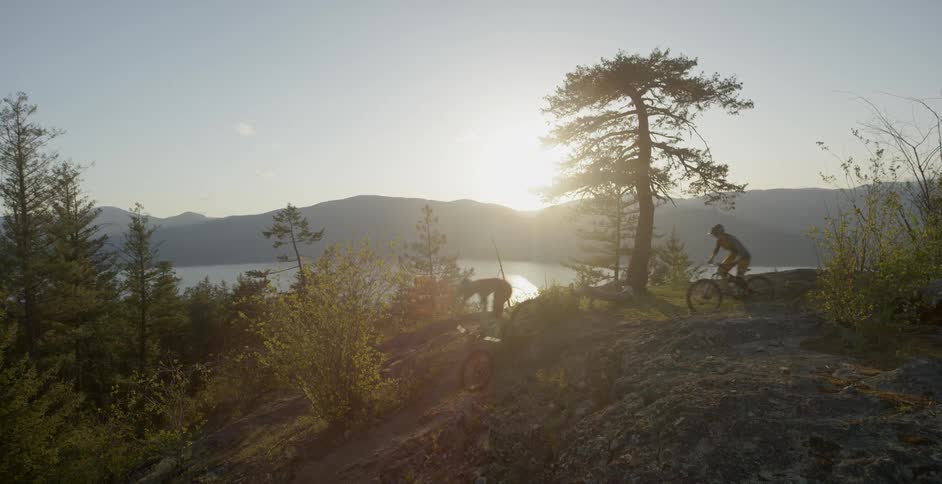 Two people ride bicycles down a hill under a blue sky