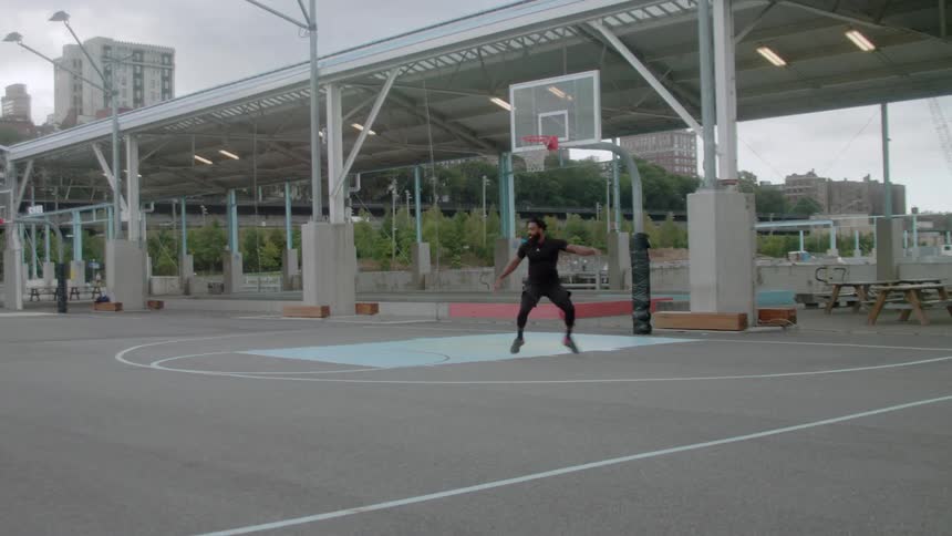 A man is practicing blocking on an empty basketball court on a cloudy day