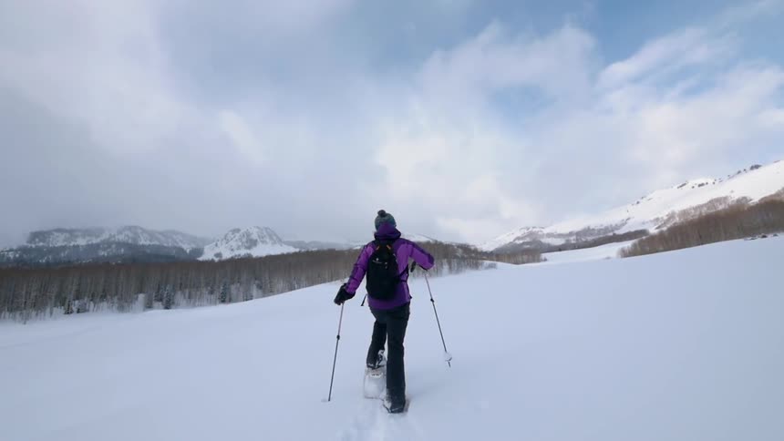 A woman is walking through deep snow wearing snow shoes