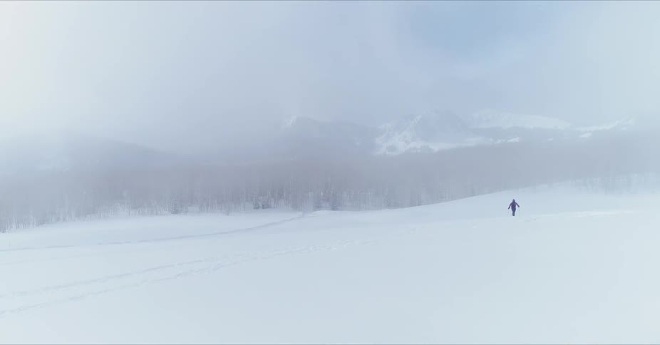Man walks through a snowy field under a blue sky