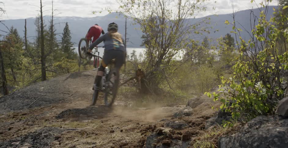 Two people are riding mountain bikes down a trail