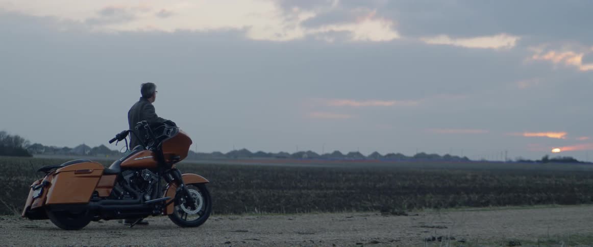 Motorcyclist is stopped in a rural field at sunset