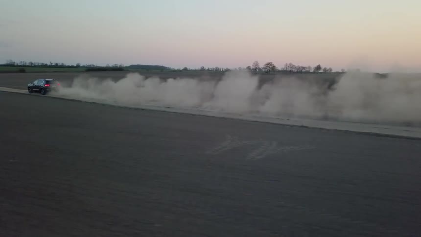 Car drives across a dirt field at sunset