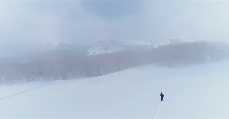 Person hiking through thick snow towards mountains