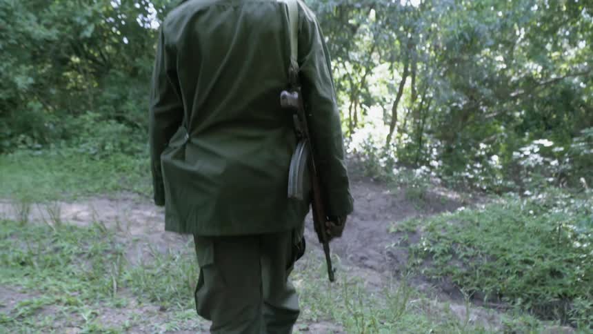 Soldier carrying a gun walks through the woods on a sunny day