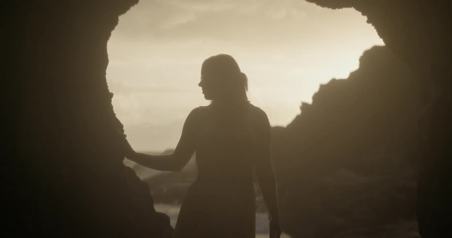 Woman stands near the mouth of a cave at sunset