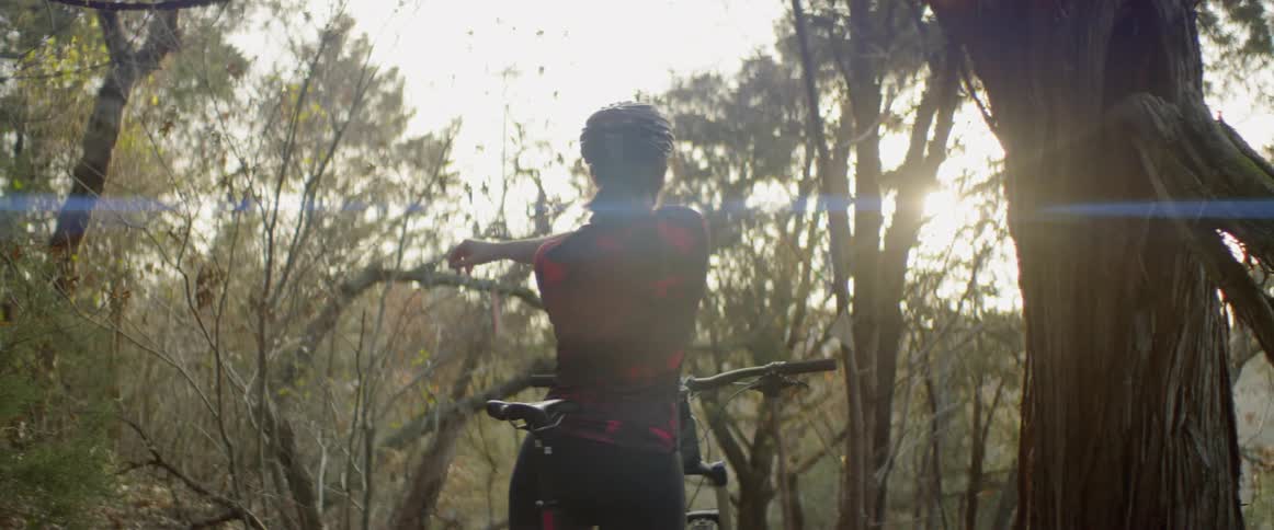 A bicyclist stops to stretch in a forest at sunset