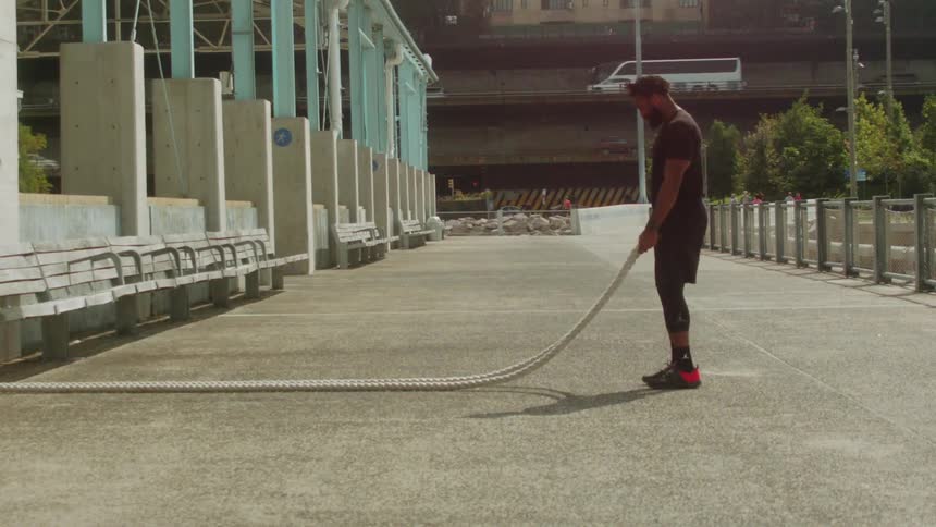 A man stretches and works out using the heavy rope outside
