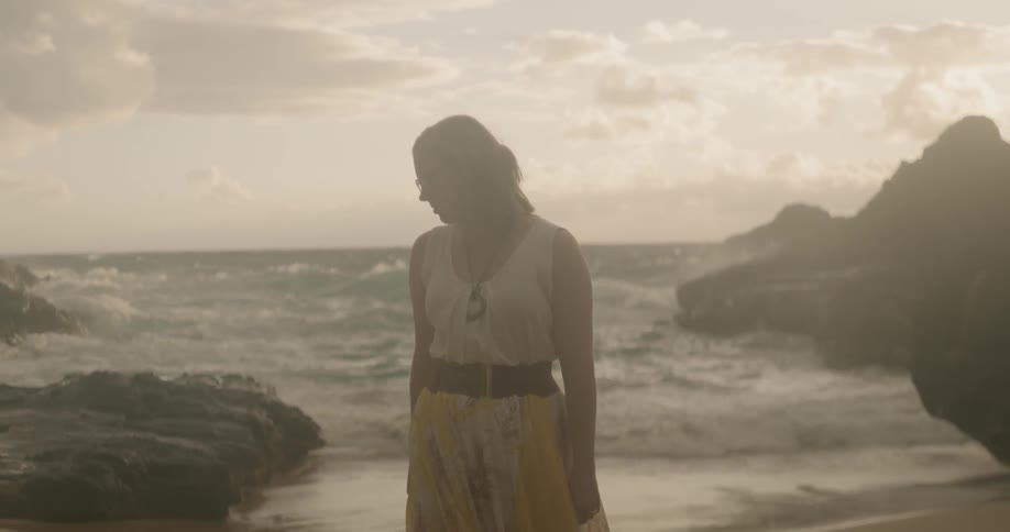 Woman stands on a beach at sunset