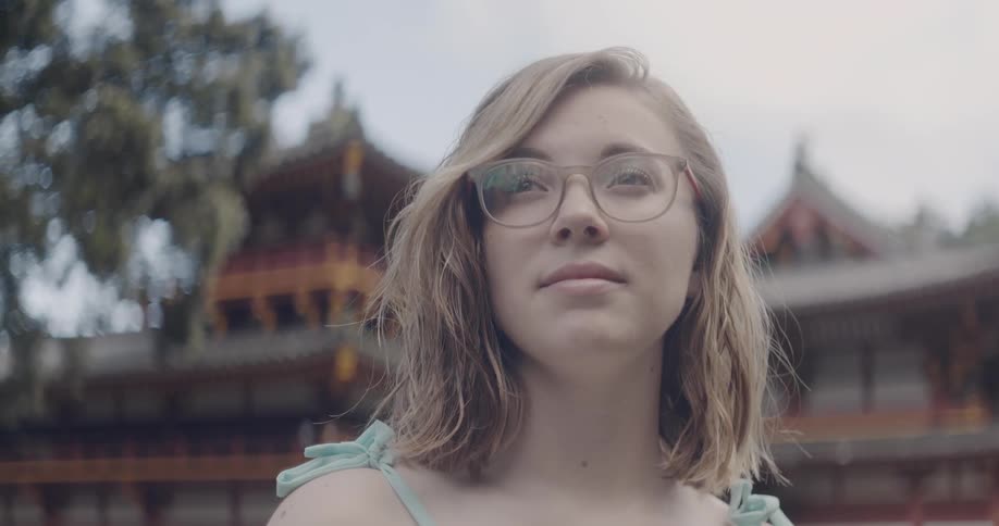 Woman wears glasses as she stands near an oriental building