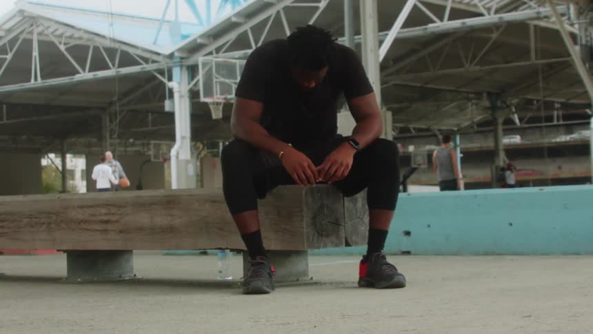 A man is sitting in thought and rest on a bench at a basketball court in daylight