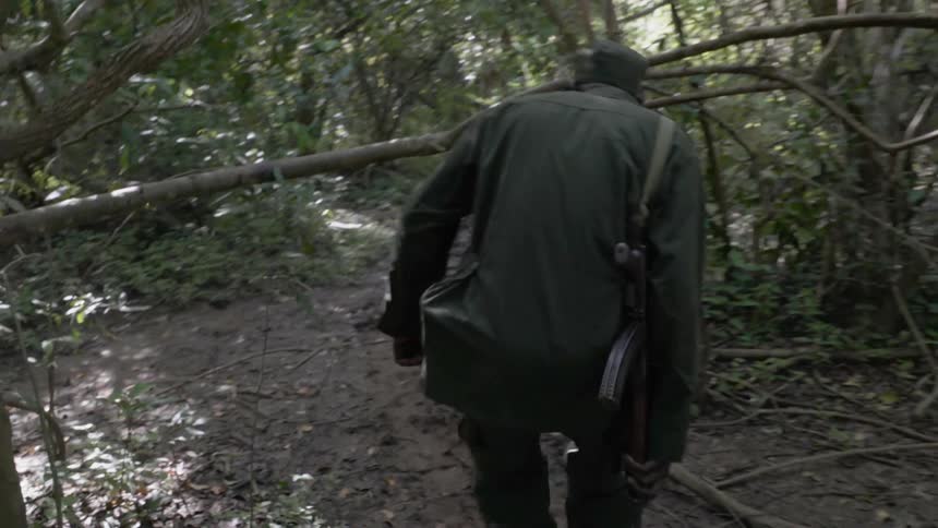 An armed soldier walks in a forest