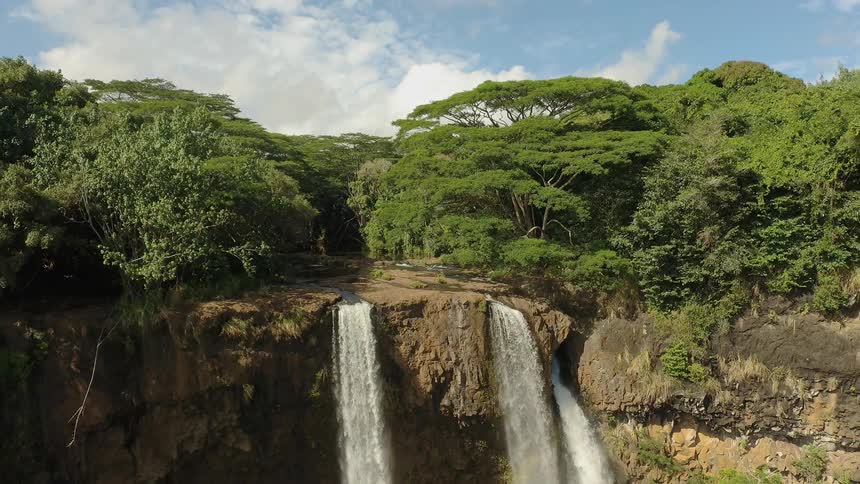 Waterfall flowing off rock cliff in front of green forest of trees