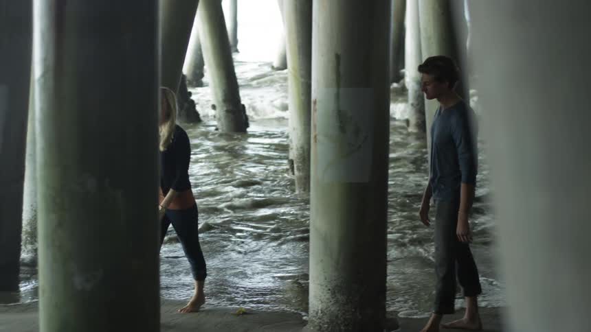 A man and woman standing under a pier talking