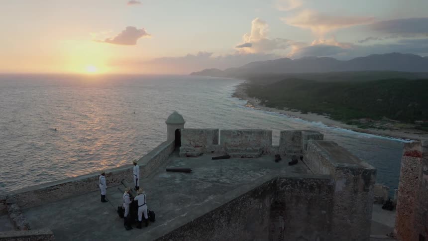 A cannon and military men on a wall by the ocean