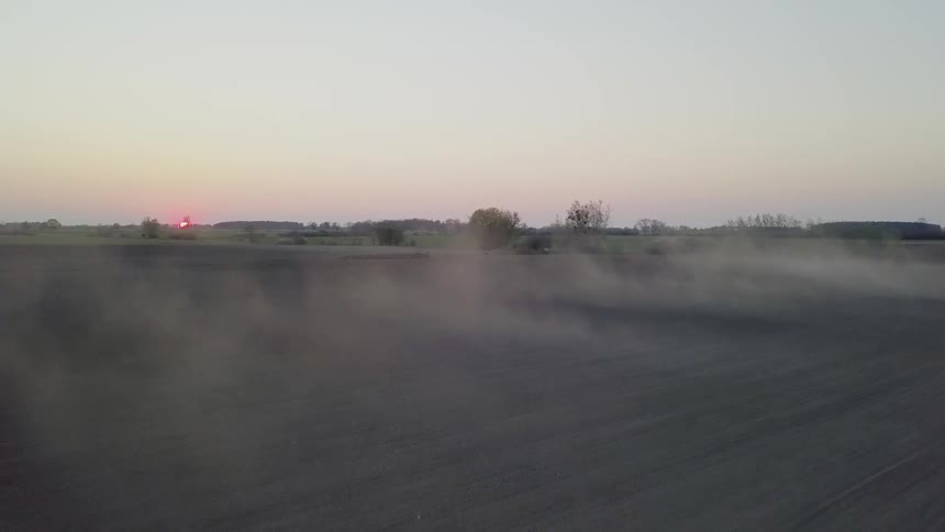 Dust billows across a field at sunset
