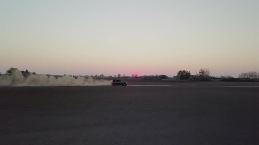 Car drives on a dirt field at sunset