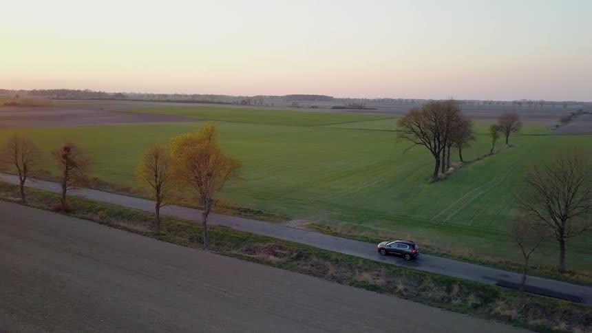 A car is parked on a rural road at sunset