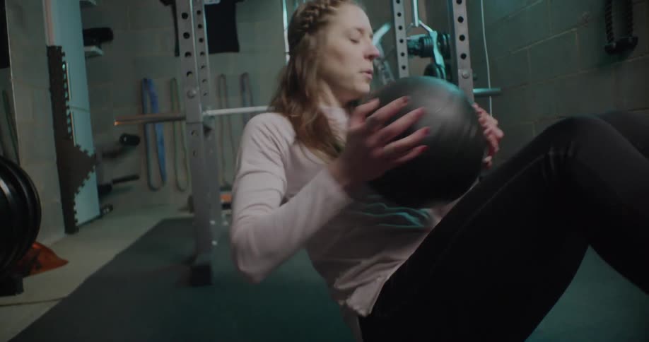 Woman sits on the floor and moves a large black ball from one side to the other