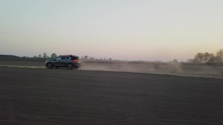 A car is driving across a dirt road at sunset