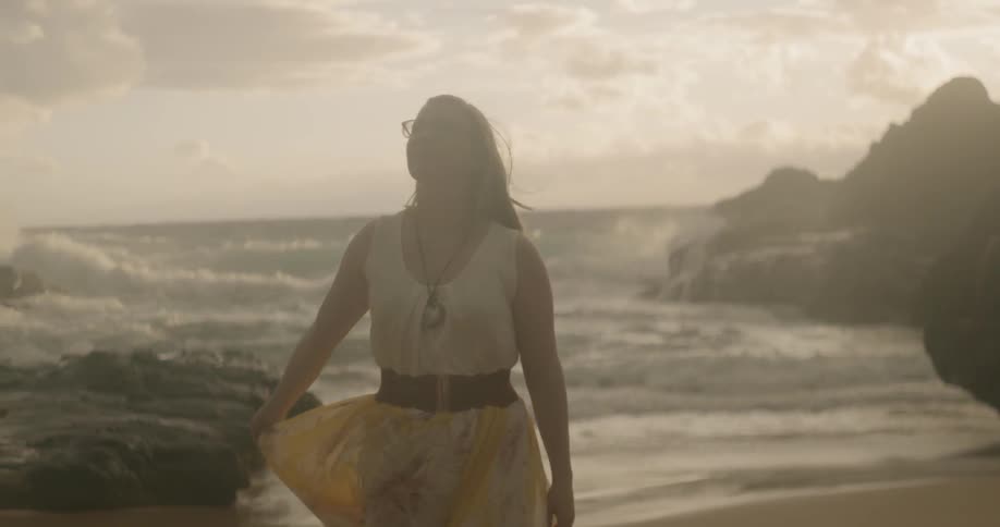Woman wearing glasses spins around as she stands near the ocean