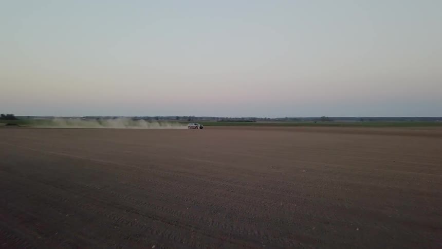 A car drives across a dirt field at sunset
