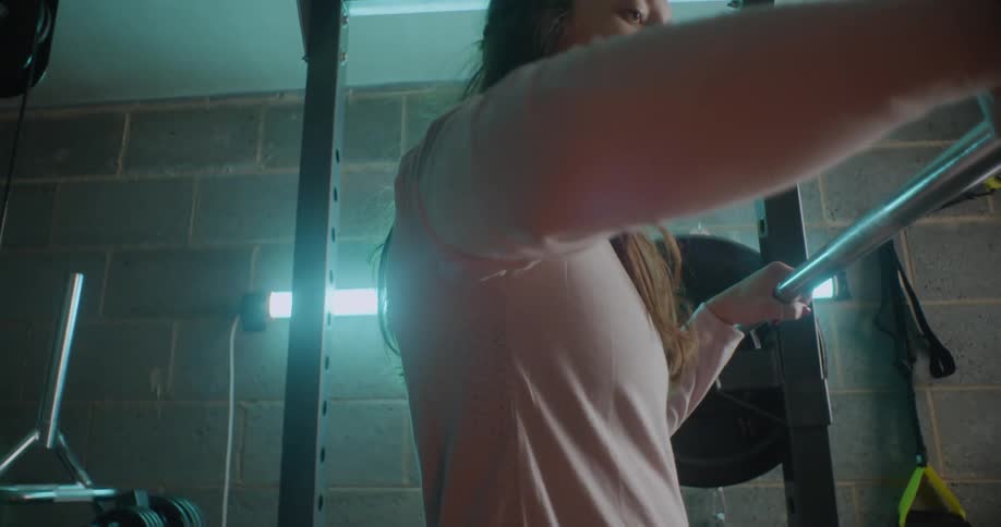 A woman is crouching some weights in the gym