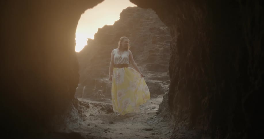 Woman stands near the mouth of a cave at sunset