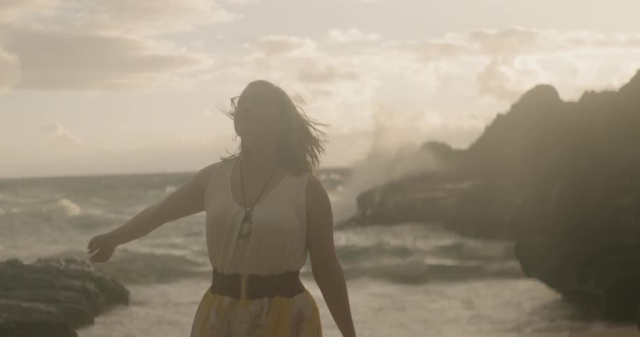 Woman on rocky shore turns in the wind