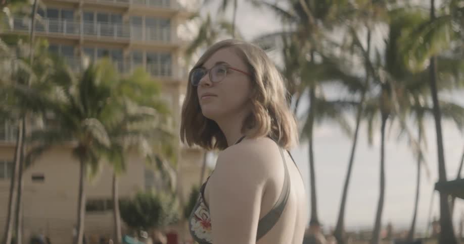 Woman walks near palm trees on a beach towards a building