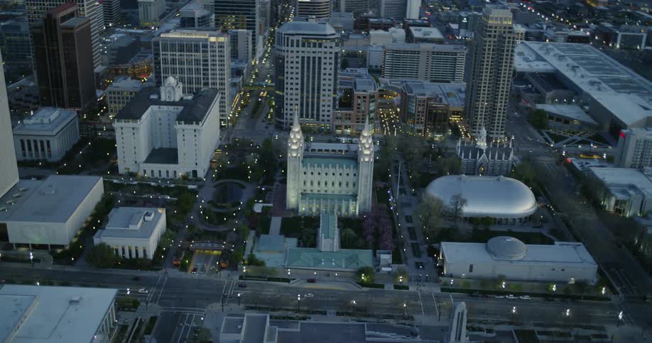 Lights are illuminating a building and adjacent streets in a city at dusk