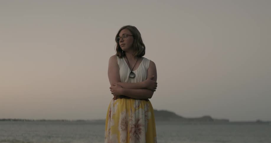 A woman is standing on a field hugging herself