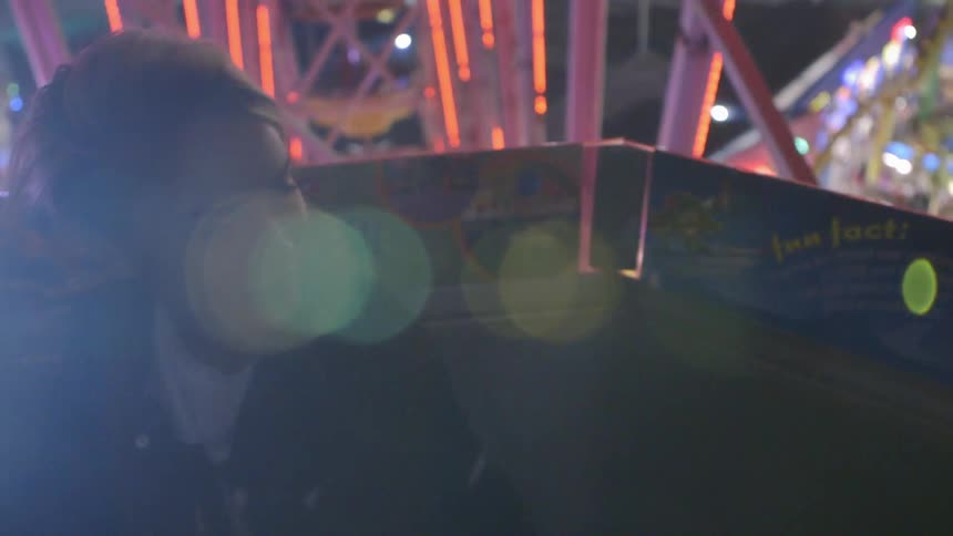 Wind blows through the hair of a girl sitting in the car of a ferris wheel