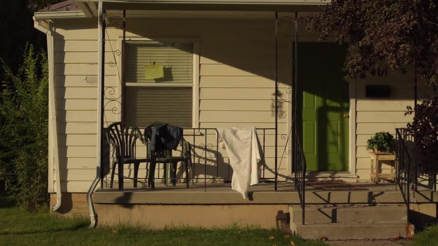 A man without a shirt is running past the porch of a house