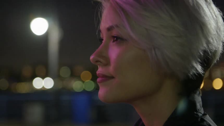 A young woman softly smiling and looking up at something in an urban area before she turns around