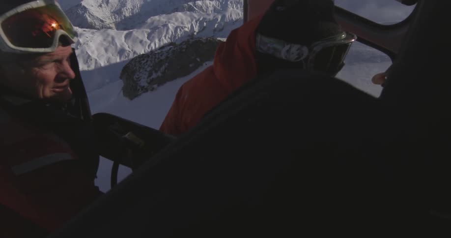 Snowboarders exit their helicopter on top of a mountain