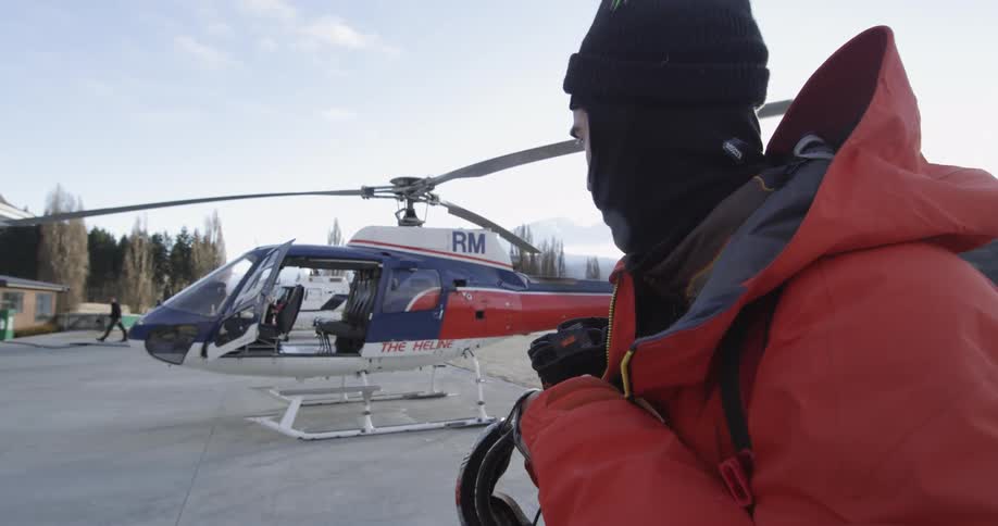 A man adjusts his coat in front of a helicopter