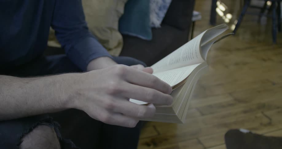 A man is sitting in a living room reading a book during the day