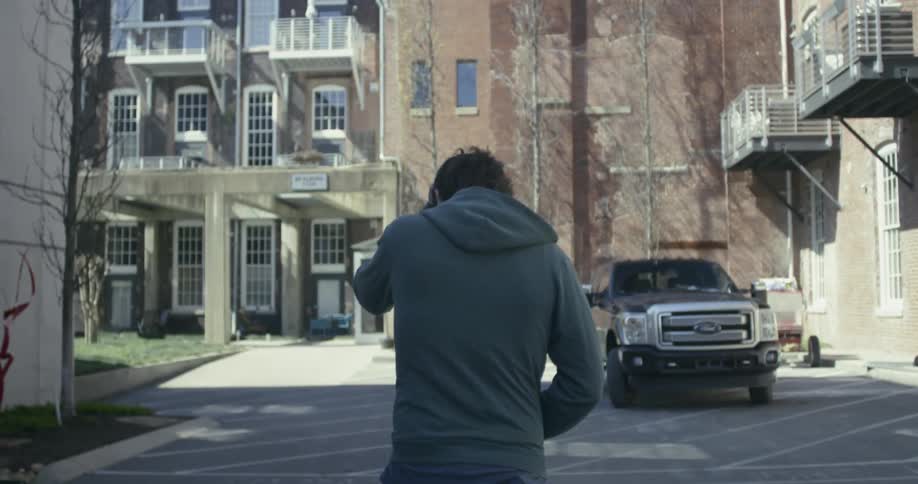 A man is brushing his hair back as he walks outside a residential complex in daylight