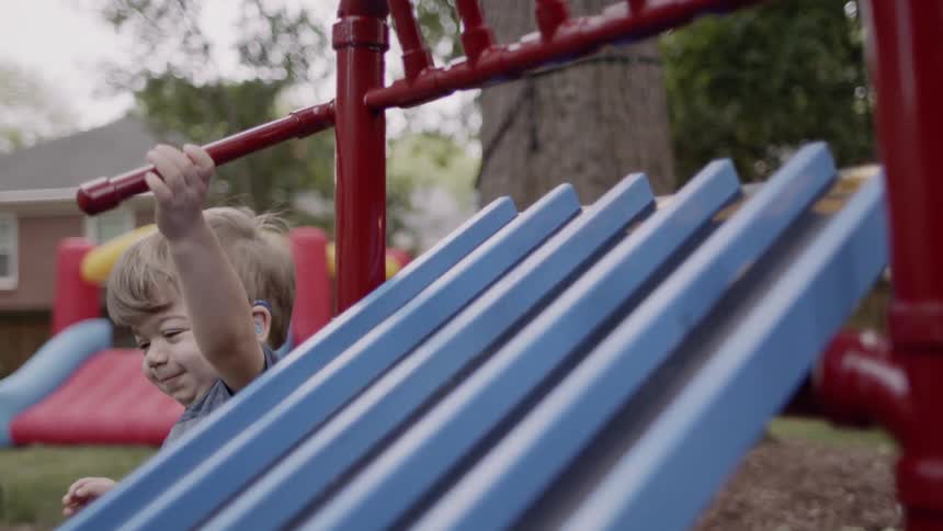 A boy is releasing toy cars down a slide outside in a backyard in daylight
